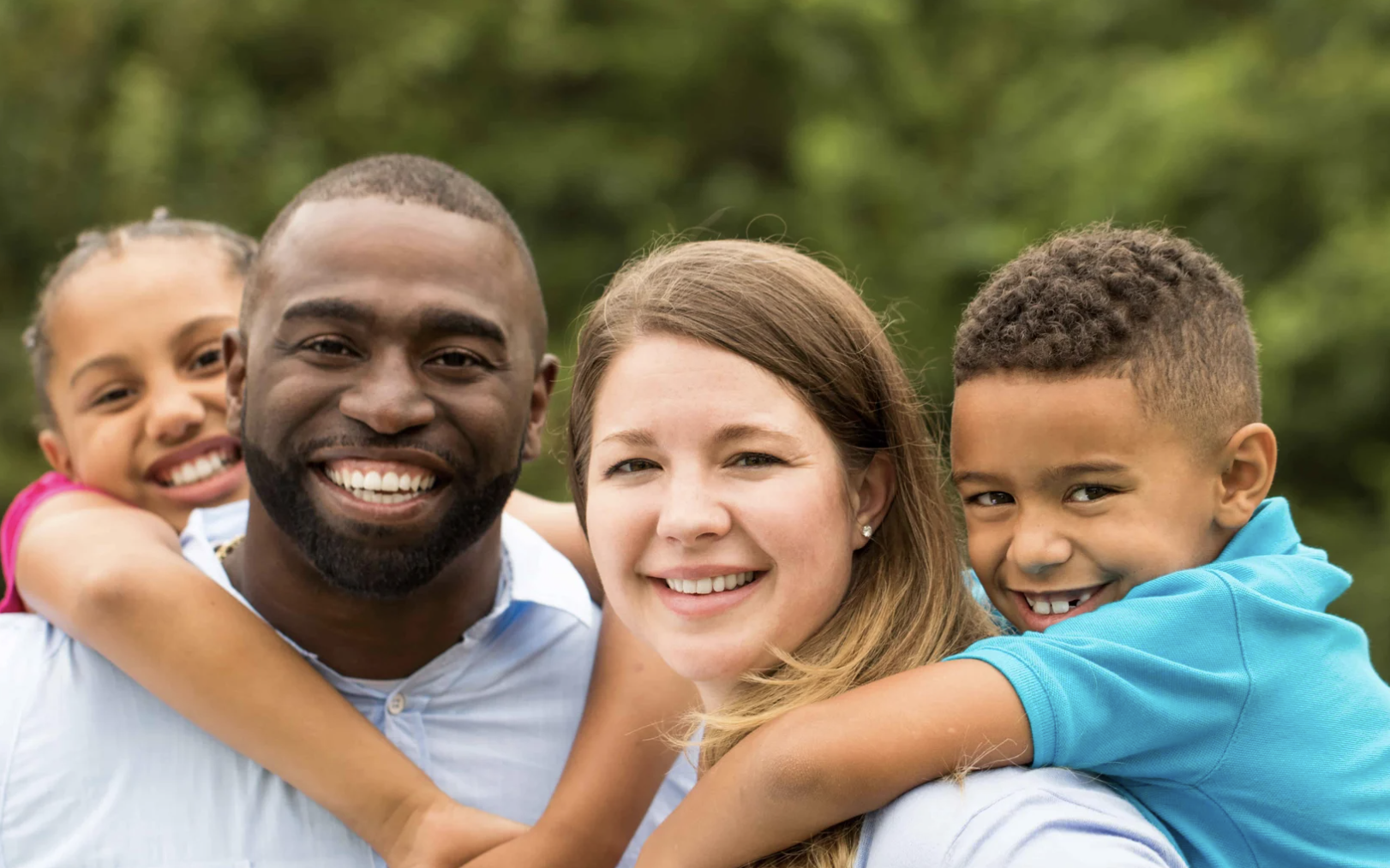 Smiling family of four — dad, mom, and two kids laughing together